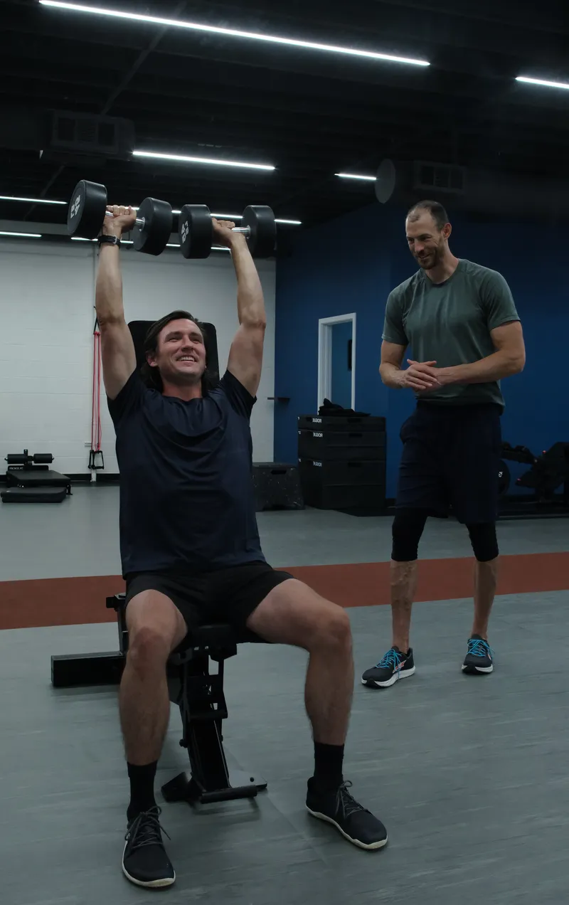 Standing overhead dumbbell press with a coach spotting